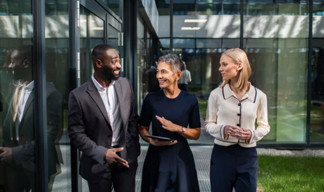 Three business professionals stand outside a modern glass office building, one holding a tablet, representing modern business practices and online directory visibility strategies.