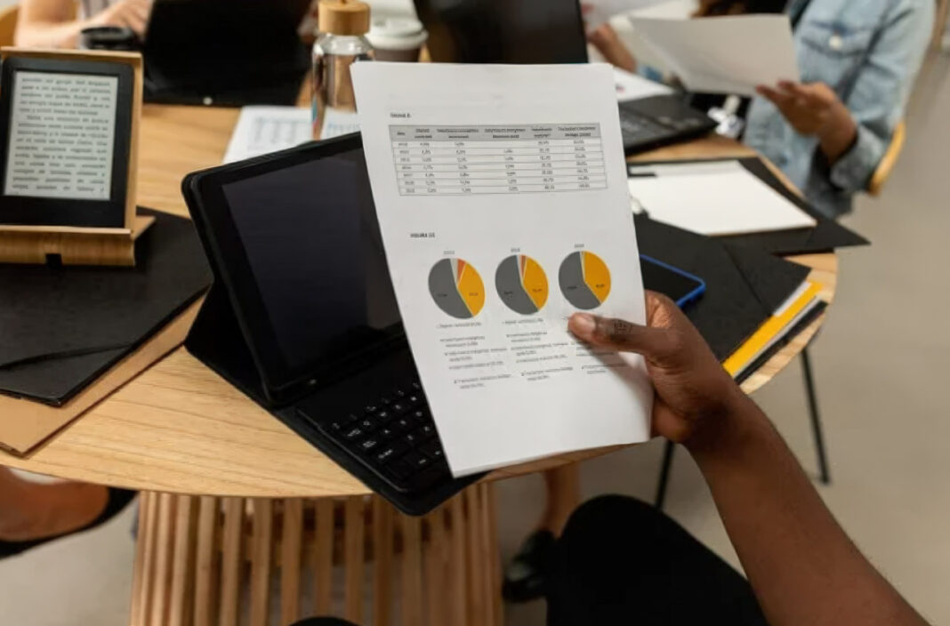 Business report with performance charts illustrates Canadian provincial directory ranking analysis Person holding a printed business report with pie charts and data tables over an office desk, representing analysis of Canadian provincial directory performance rankings.