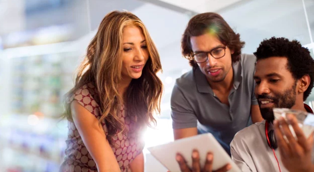 Three business professionals collaborate around a tablet in a modern office with natural light, representing directory software platform development and entrepreneurial innovation.