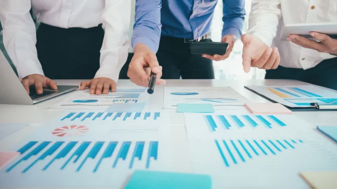 Business team members review printed bar charts and performance graphs on a conference table during an analytics meeting related to provincial directory rankings.