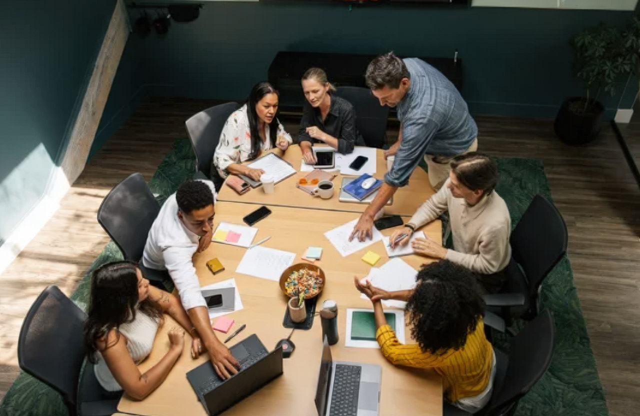 Overhead view of business team collaborating around a conference table with laptops and documents, representing the collaborative approach to building community-based directories.