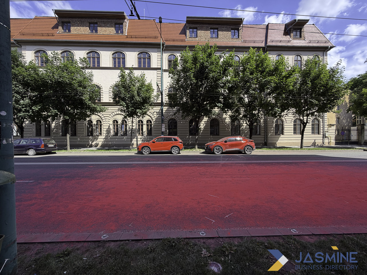Classical European building with arched windows and tile roof along tree-lined street in Timișoara, illustrating the type of neighborhood landmarks that anchor local business authority.