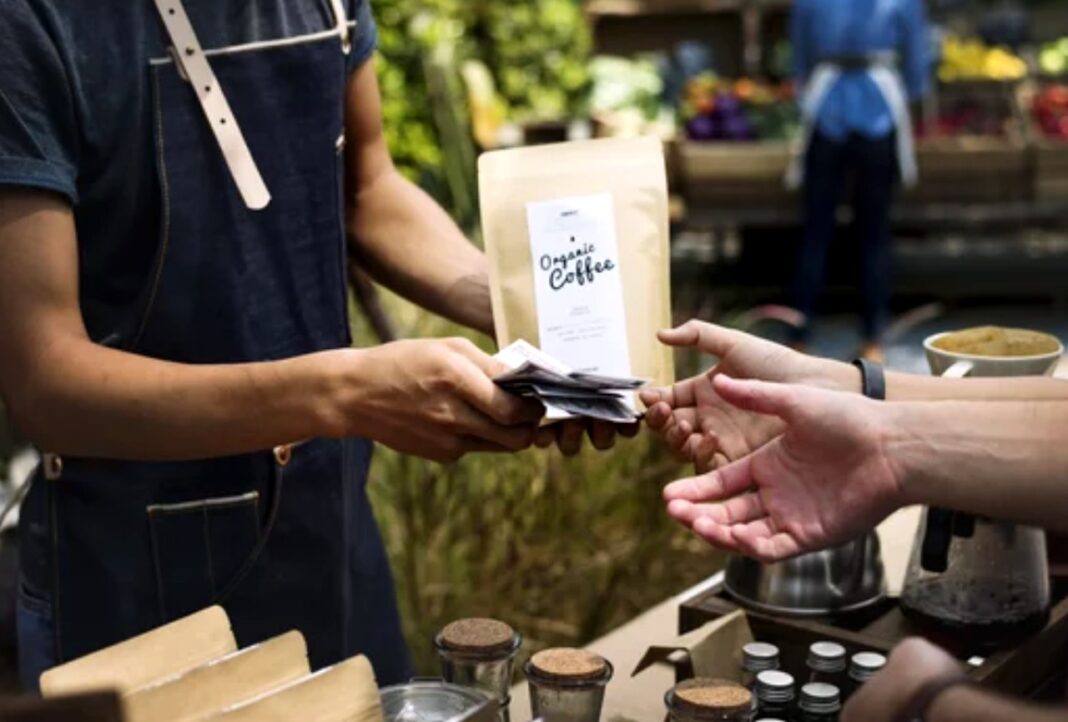Small business transaction illustrates the sponsorship model supporting niche community vendors A coffee vendor hands a payment terminal to a customer at an outdoor booth, representing direct commerce in niche community markets sustained by local patronage.