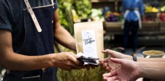 The Return of the Sponsorship Model: Supporting Niche Communities A coffee vendor hands a payment terminal to a customer at an outdoor booth, representing direct commerce in niche community markets sustained by local patronage.