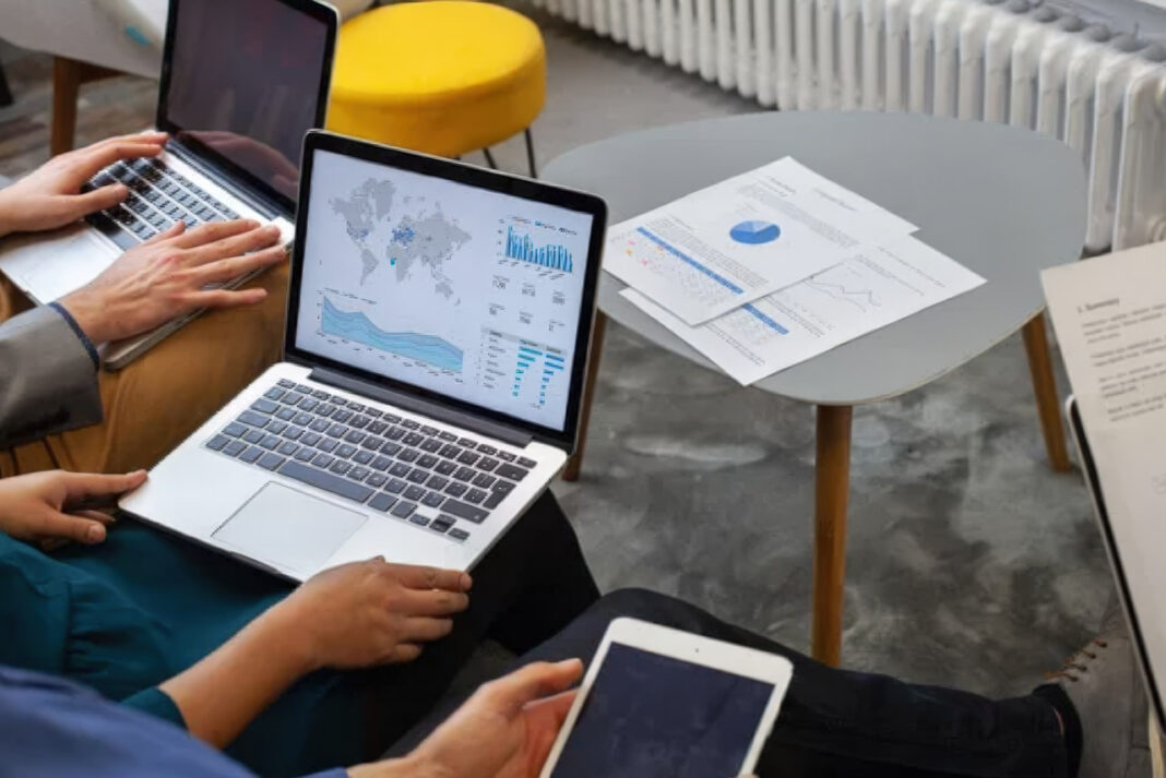 Business professionals analyzing directory performance metrics and data dashboards Two professionals collaborate at a desk with laptops and printed data visualizations, reviewing analytics dashboards relevant to directory performance measurement.