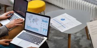 Australian Directory Analytics That Matter Most Two professionals collaborate at a desk with laptops and printed data visualizations, reviewing analytics dashboards relevant to directory performance measurement.