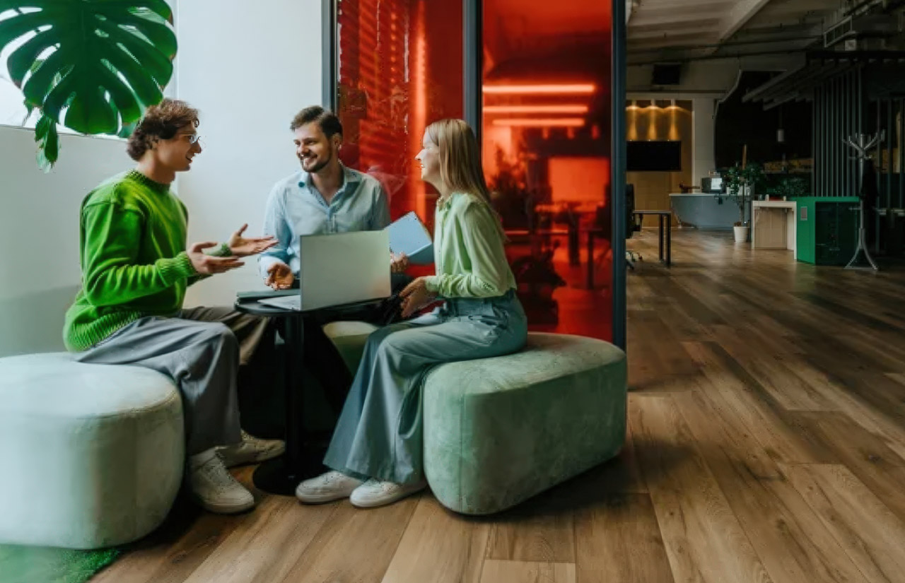 Three professionals collaborate around a laptop in a modern office with orange illuminated panels, representing the community-focused approach to building authoritative directories.