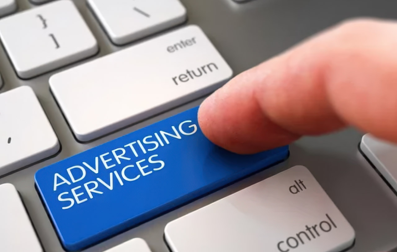 Close-up of a computer keyboard with a bright blue 'ADVERTISING SERVICES' key being pressed by a finger, representing accessible digital marketing tools for local service providers.