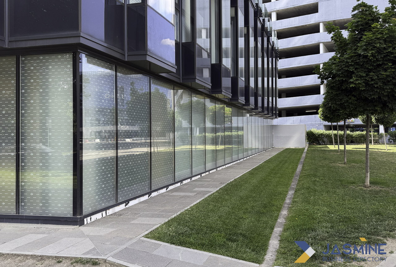 Modern glass-facade residential building with professionally landscaped lawn and young trees along the walkway, illustrating quality property maintenance and landscape design.