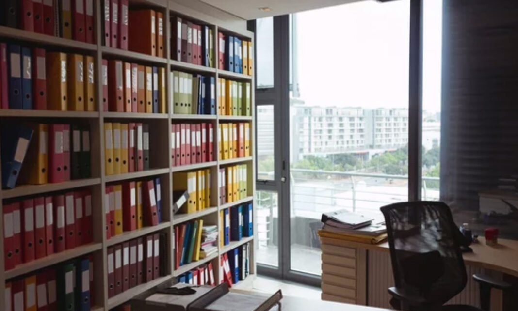 Organized office filing system illustrates industry-specific directory categorization and professional information management Modern office with floor-to-ceiling shelves holding colorful organized binders and folders, representing systematic categorization used in industry-specific business directories.