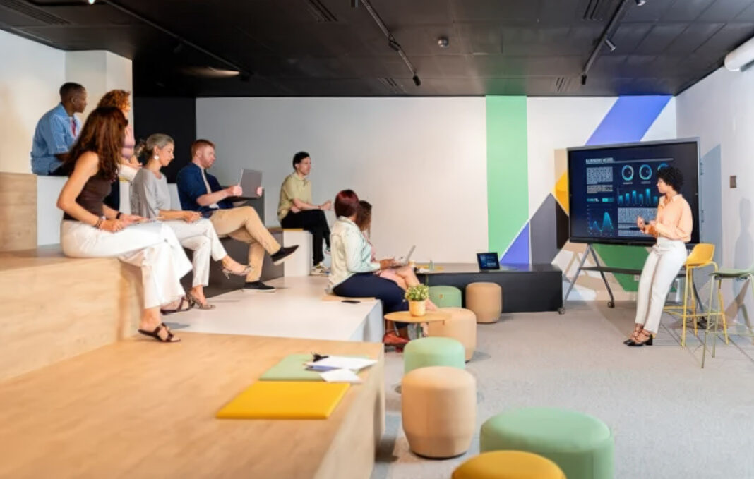 Modern presentation demonstrates predictive customer service analytics to business team A woman presents data analytics on a large screen to seated business professionals in a modern office, illustrating predictive customer service strategies.