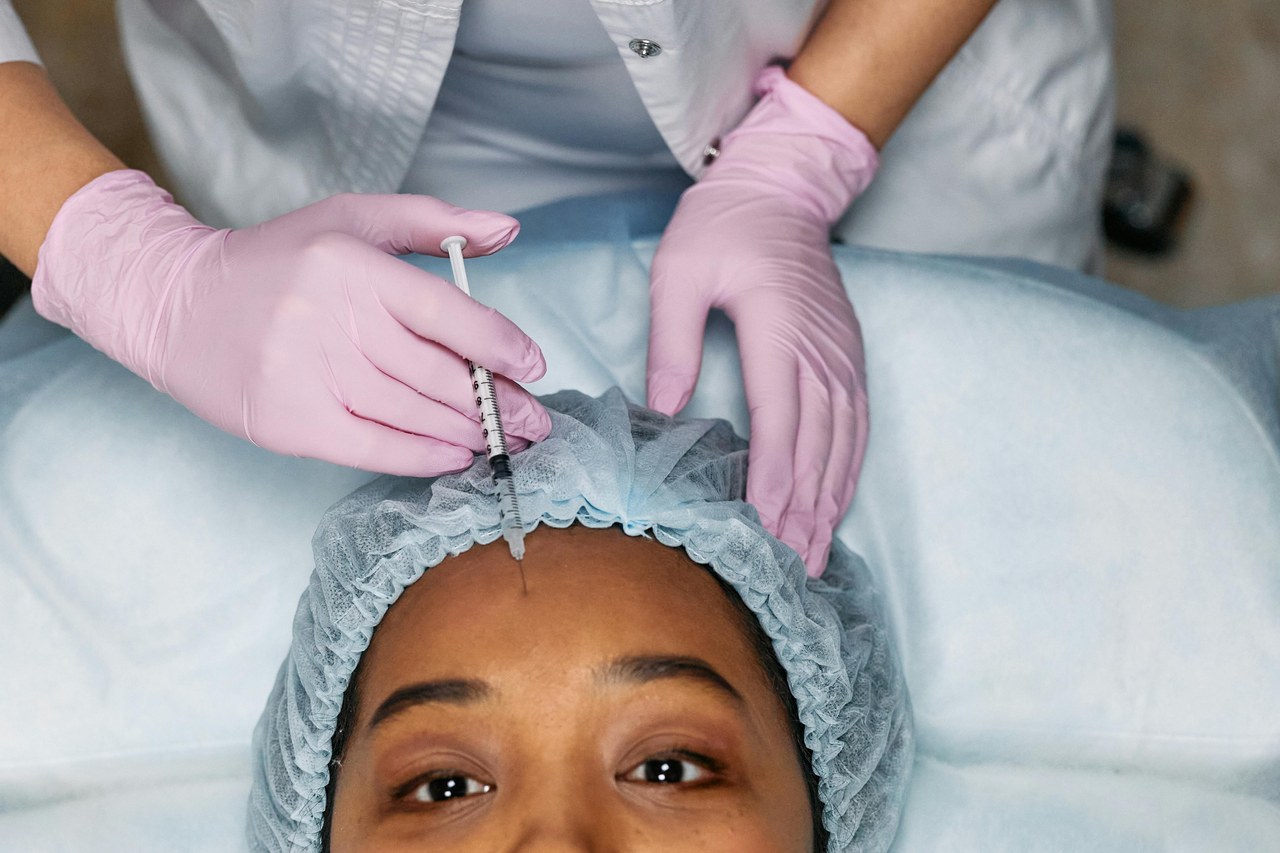 Overhead view of a practitioner in pink gloves administering a cosmetic injection to a patient's forehead, illustrating skin injectable procedures.