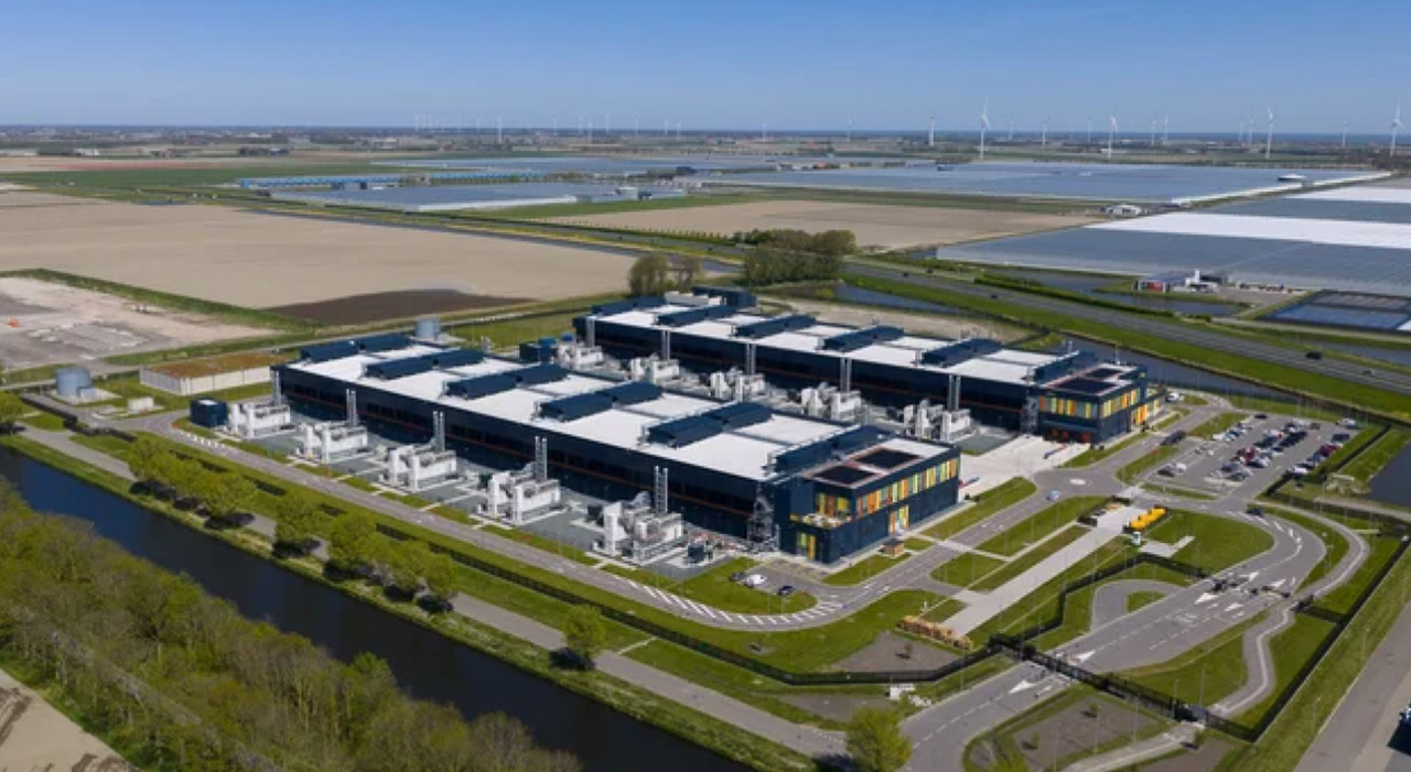 Aerial view of a modern data center complex with blue industrial buildings surrounded by water channels, illustrating the physical infrastructure supporting digital business directories and AI search systems.