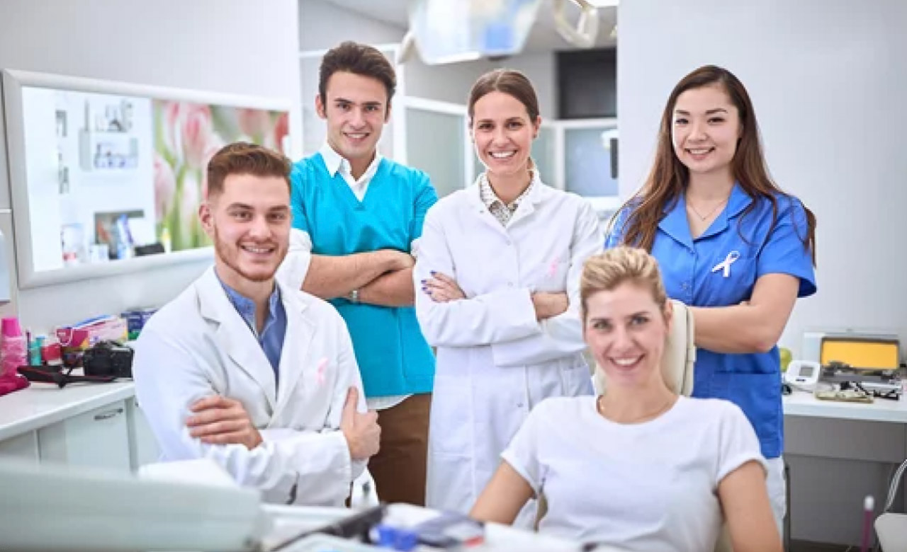 Five dental professionals in clinical attire pose in a modern dental office, representing the collaborative team approach essential to effective preventative dental care.