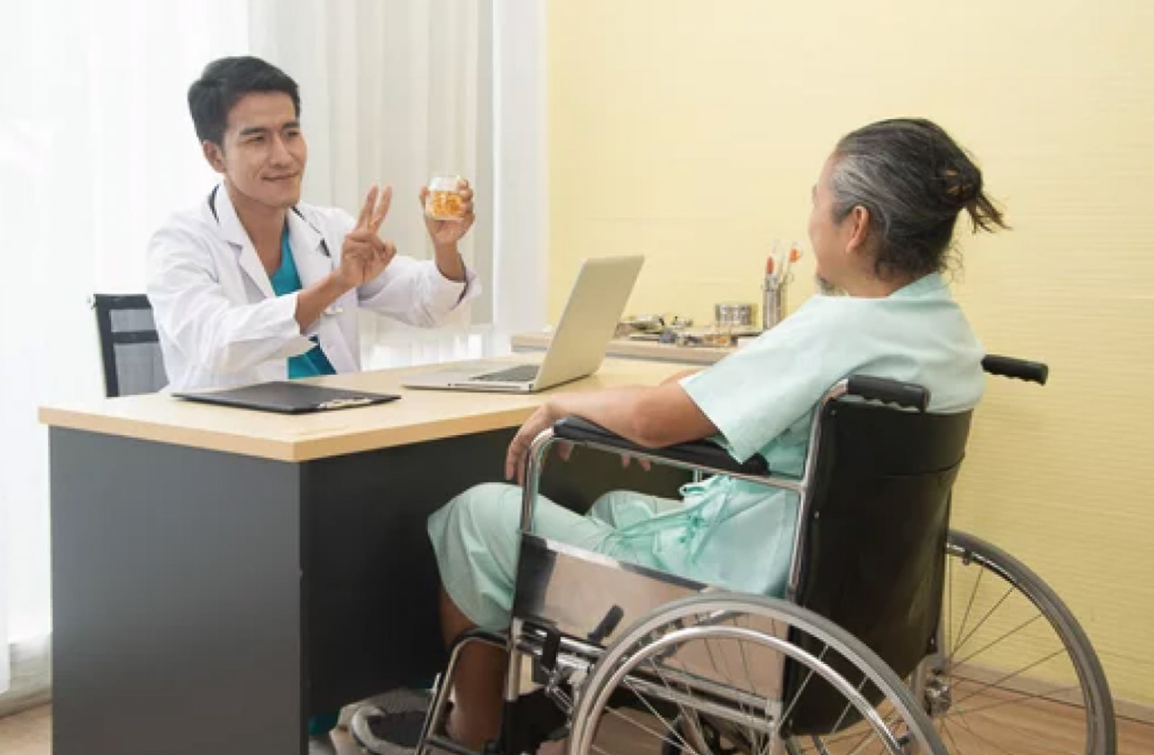 Doctor in white coat consults with a patient in a wheelchair at a desk in a medical office, demonstrating accessible and inclusive healthcare service delivery.