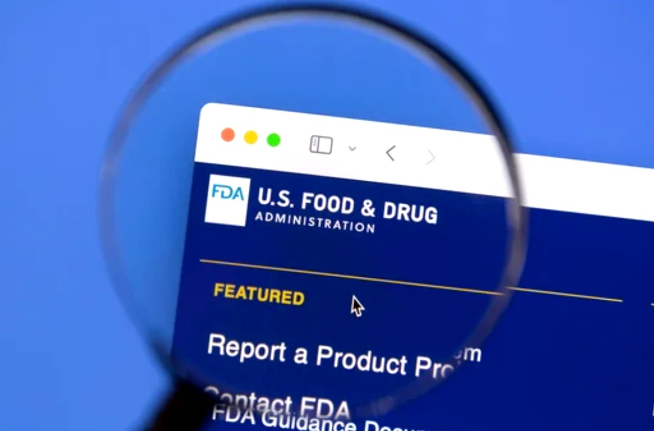 A magnifying glass examines the FDA website homepage on a computer screen, illustrating the scrutiny applied when evaluating medical directory link credibility.