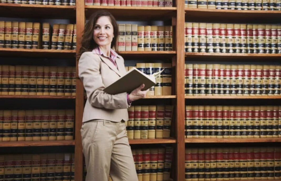 Legal professional in library represents attorney online visibility and directory marketing strategies Female attorney in beige suit holds an open book in a law library with floor-to-ceiling shelves, illustrating legal professional visibility and directory marketing.