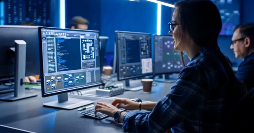 IT professional reviewing code at workstation during technical audit process Female IT professional wearing glasses works at computer workstation with multiple monitors displaying code, representing technical audit workflow and website evaluation processes.