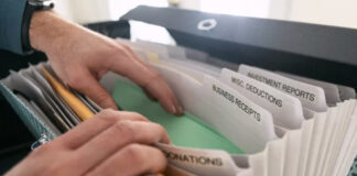 How do directories make money? Hands retrieve a green folder from an accordion file organizer with labeled tabs for business receipts and financial categories, representing organized revenue tracking systems.
