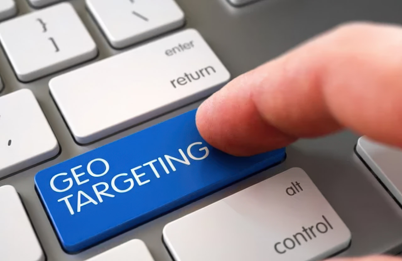 Finger pressing a bright blue geo targeting key on a computer keyboard, representing location-based customer targeting capabilities for local businesses.