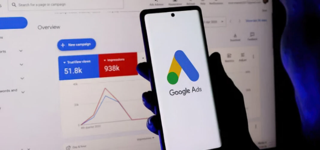 Google Ads interface illustrating display advertising platform before establishing directory citation foundation Hand holding smartphone with Google Ads logo in front of desktop monitor displaying advertising dashboard metrics, representing display advertising tools discussed in directory citation strategy.
