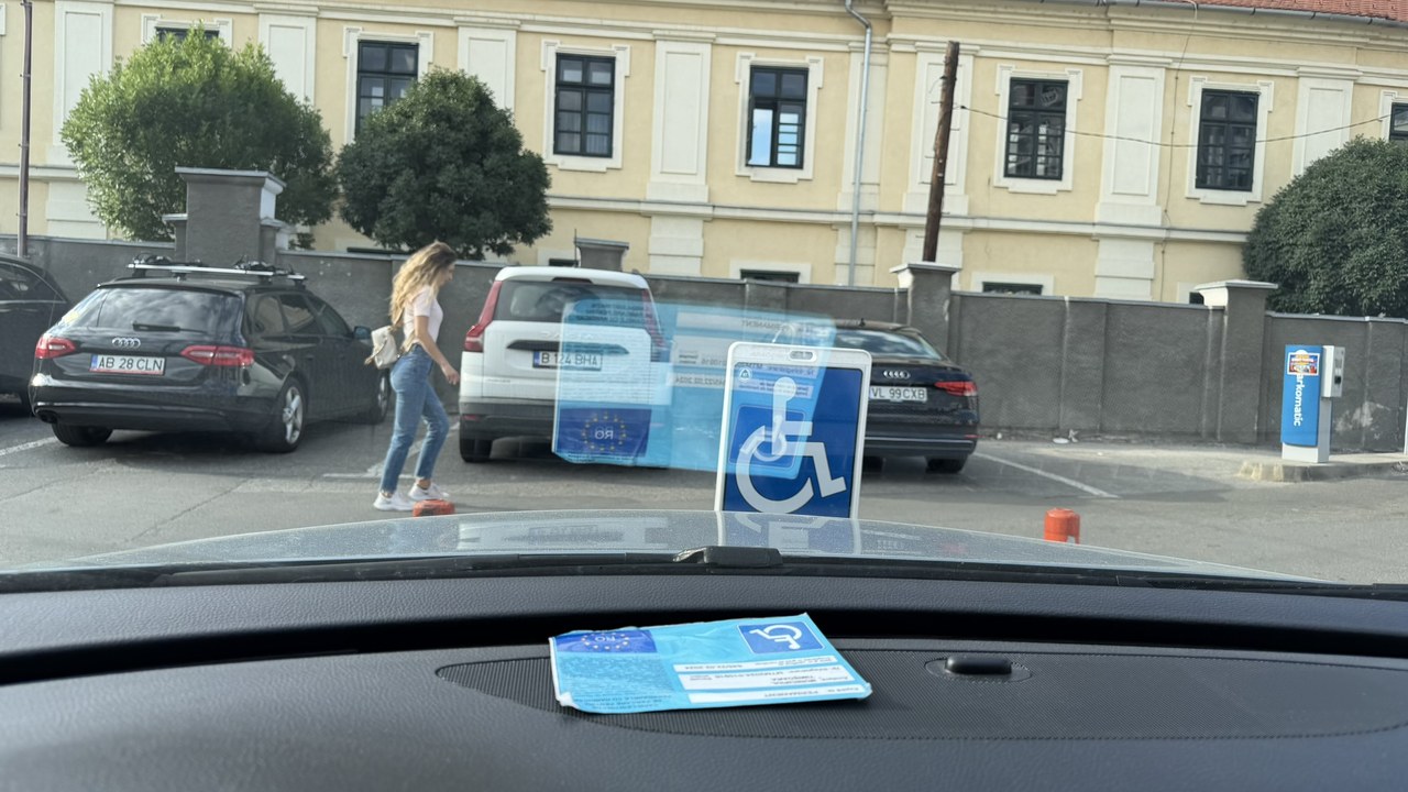 A blue handicapped parking permit with wheelchair symbol sits on a car dashboard overlooking a parking area, illustrating accessibility attributes that help users filter business listings.