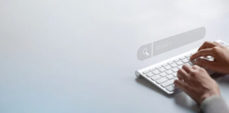 Hands typing on a white keyboard with a translucent search bar overlay, illustrating the digital interface used in AI-driven keyword research processes.