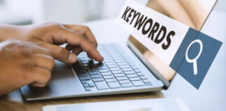 The Easiest Way to Find Keywords Hands typing on a silver laptop keyboard with a keywords sign and magnifying glass icon visible, representing methods for finding and organizing directory search terms.