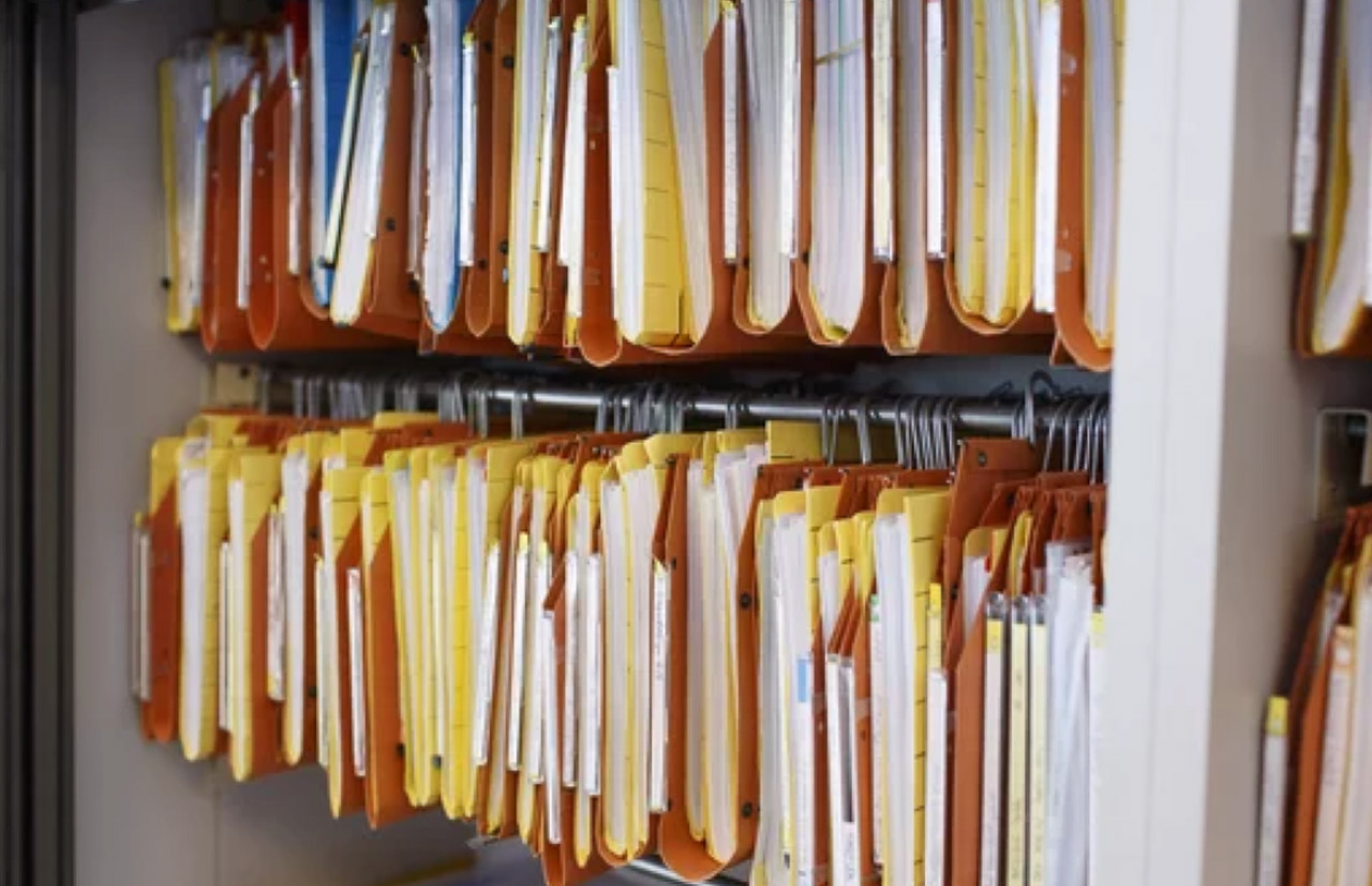 Rows of color-coded hanging file folders suspended on metal racks demonstrate systematic organization principles relevant to database schema and table structure optimization.