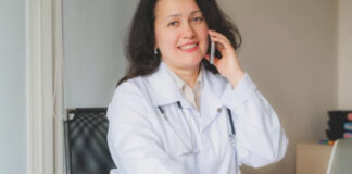 Optimizing Your Directory for Voice Search: A Guide to Featured Snippets Healthcare professional in white lab coat smiles while speaking on smartphone at desk with laptop, representing voice search accessibility for medical directory listings.
