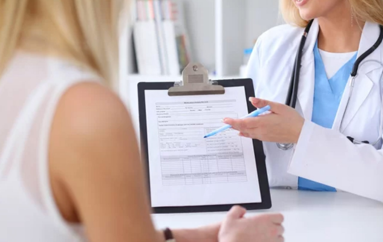 Doctor in white coat shows medical form on clipboard to patient during consultation, illustrating patient-centered care in modern outpatient clinics.