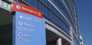 How highly regulated industries are adapting their digital marketing strategy in 2026 Hospital directional signage with emergency indicators and facility directories stands before a modern glass tower, illustrating effective exterior branding that makes a location recognizable.