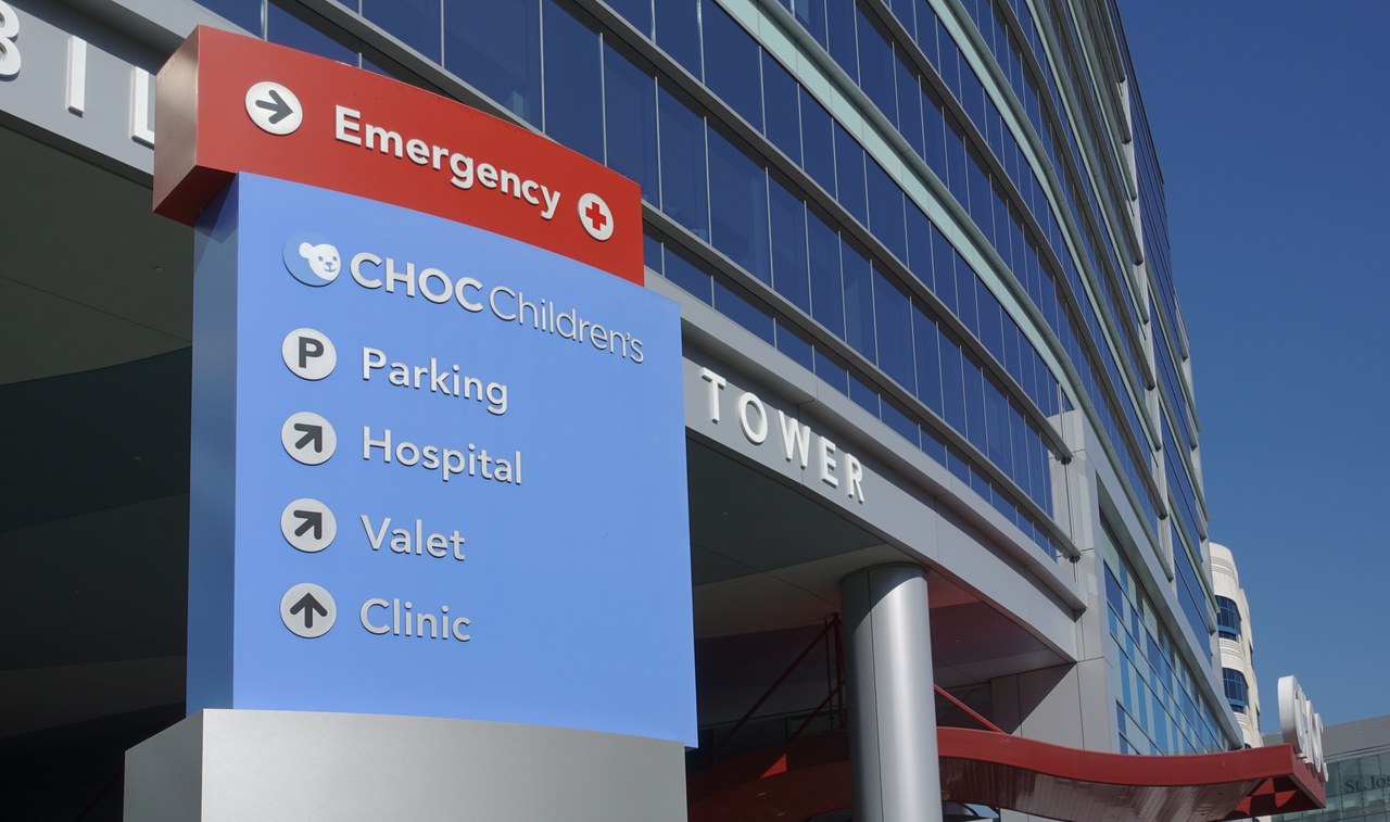 Hospital directional signage with emergency indicators and facility directories stands before a modern glass tower, illustrating effective exterior branding that makes a location recognizable.