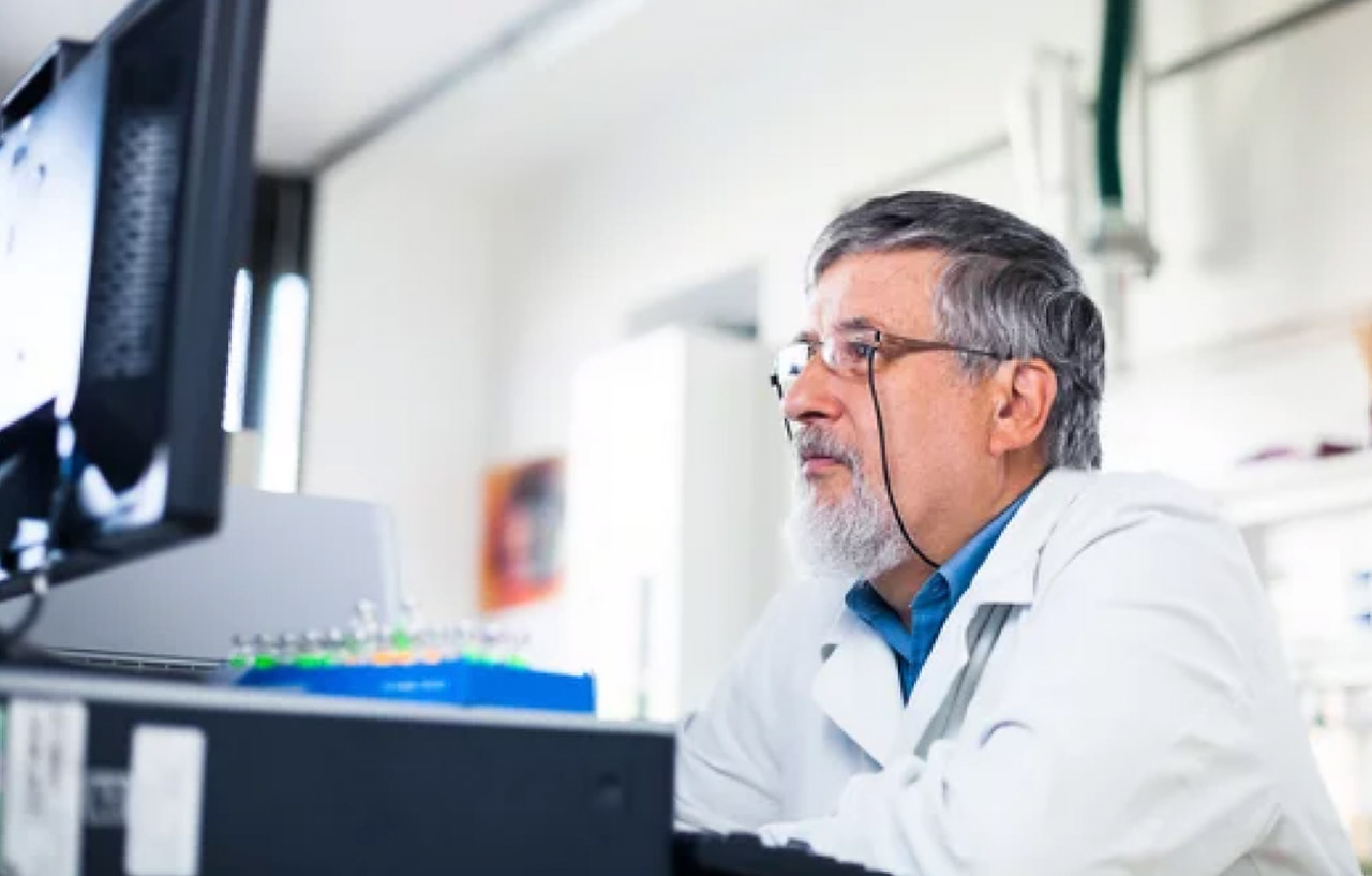 A scientist in a white lab coat works at a computer workstation in a modern laboratory, representing secure data analysis practices in privacy-preserving technology.