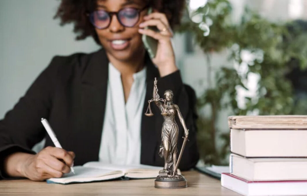 Law office setting symbolizes professional legal services and local directory visibility Bronze Lady Justice statue on a law office desk with stacked books and attorney on phone in background, representing regional legal directory services.