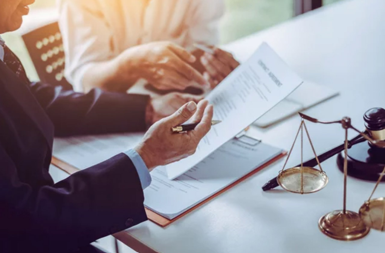 Two business professionals review legal documents at a white table with a brass justice scale and gavel, illustrating the client consultation services small law firms promote through business directories.