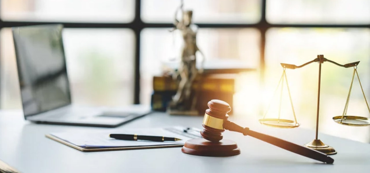 Legal office desk with wooden gavel, brass scales of justice, and laptop arranged on white surface, representing attorney directory platforms and legal professional visibility.
