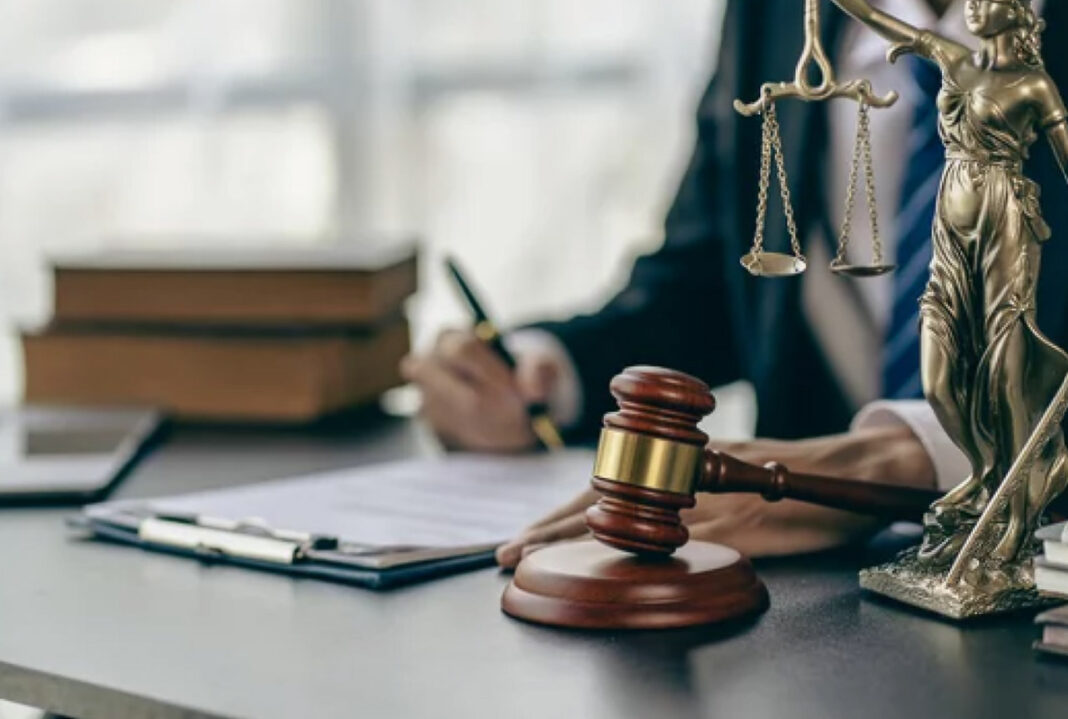 Legal workspace symbols represent small law firms building credibility through professional directories Wooden gavel and Lady Justice statue on a law office desk with attorney working in background, symbolizing small firms establishing professional presence.