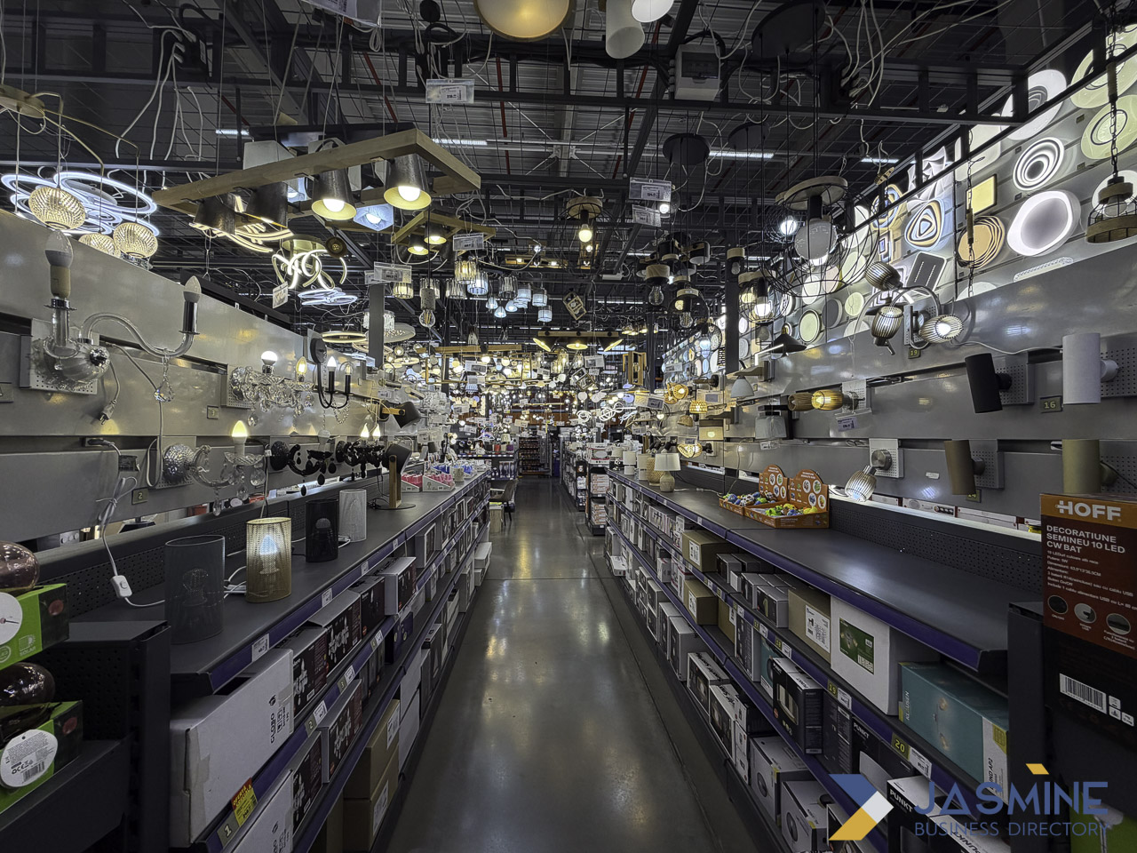 Wide view of a lighting showroom interior with illuminated fixtures hanging from the ceiling and packaged products on shelves, illustrating commercial lighting options for modern workplace design.