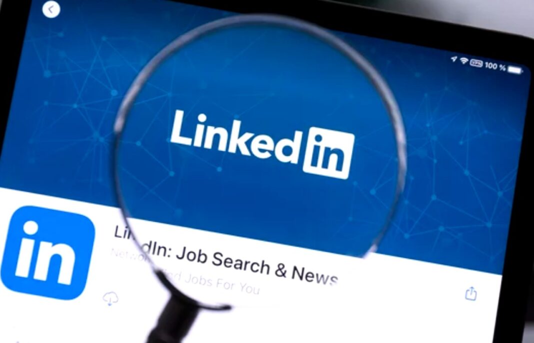 Professional networking platforms like LinkedIn play a role in digital link building strategies Magnifying glass held over a tablet displaying the LinkedIn app interface with logo and job search text, representing professional networking tools used in link building strategies.
