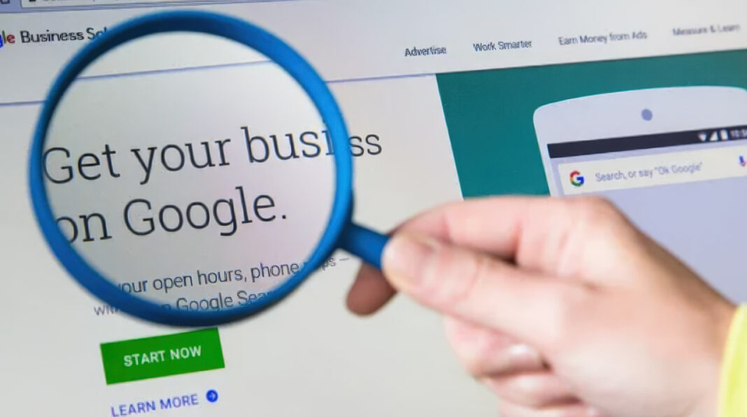 Close examination of digital marketing content illustrates shift toward brand measurement metrics Hand holding magnifying glass examining Google business promotion on computer screen, symbolizing the detailed analysis of brand measurement replacing traditional click-through metrics.