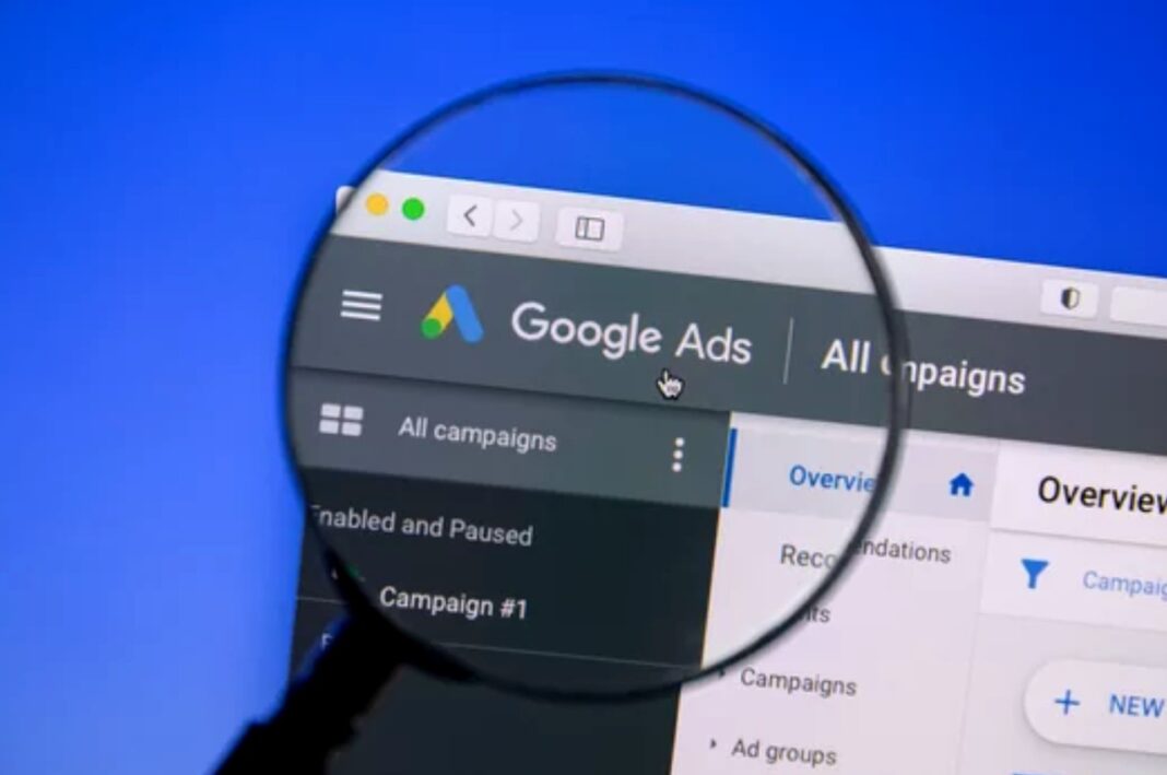 Examining Google Ads interface represents visual search advertising optimization strategies A magnifying glass focuses on a Google Ads interface displayed on a computer screen, symbolizing the scrutiny and optimization required for visual search advertising campaigns.