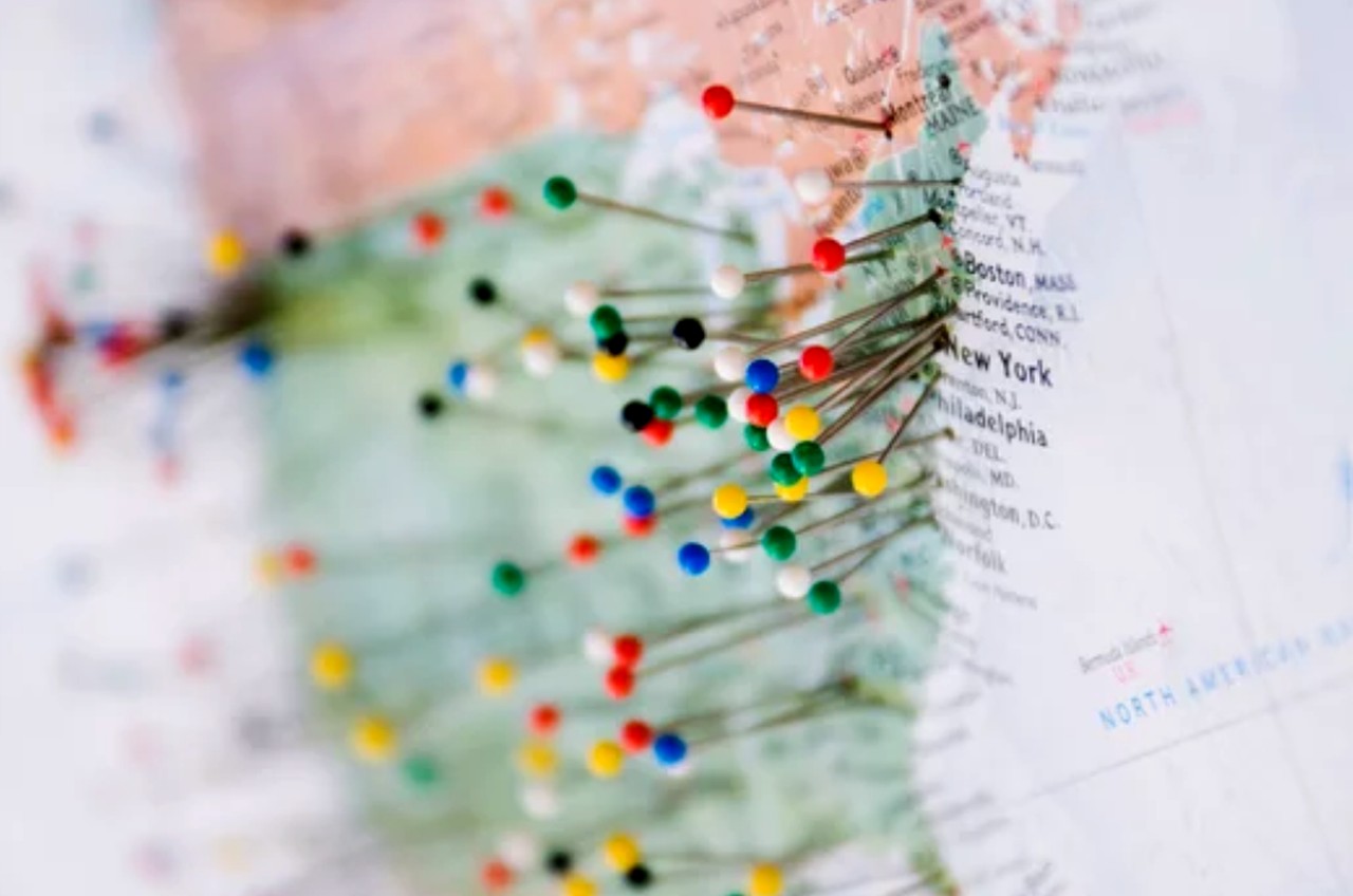 Colored pushpins mark multiple locations on a northeastern US map with connecting thread lines, illustrating multi-state directory listing management strategies.