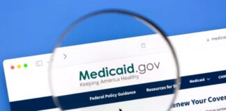Magnifying glass over Medicaid.gov website on computer screen, symbolizing examination of government assistance programs for reducing prescription medication costs.