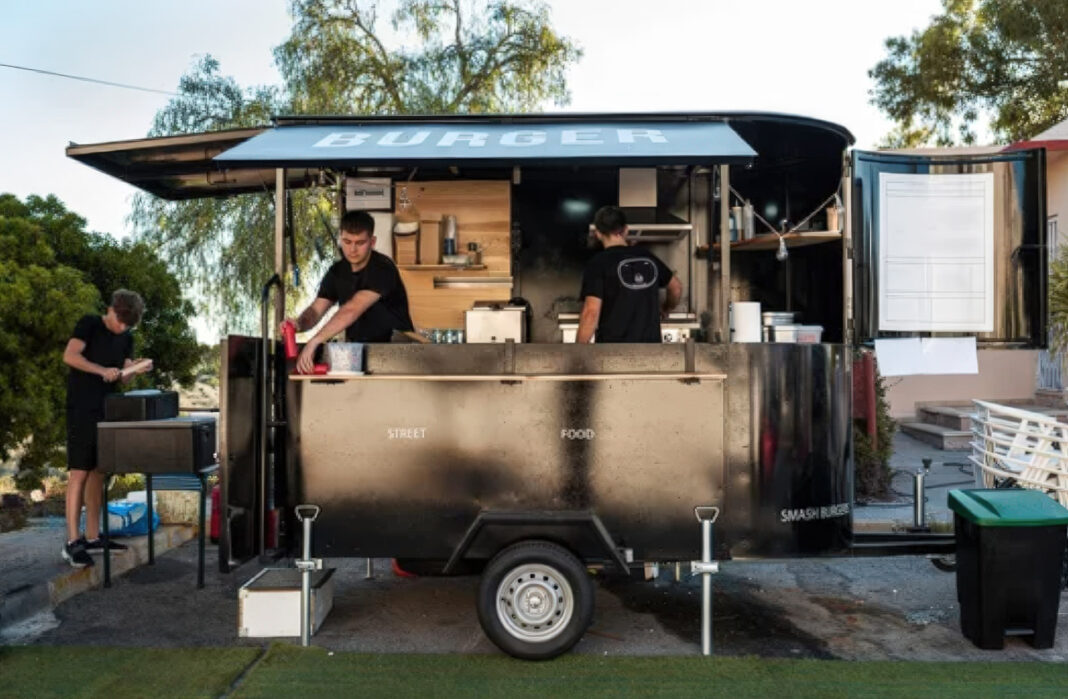 Mobile food trailer illustrates local SEO opportunities for businesses operating without a physical storefront Black mobile food trailer with burger signage and two staff members serving customers, exemplifying a mobile business that operates without a traditional storefront location.