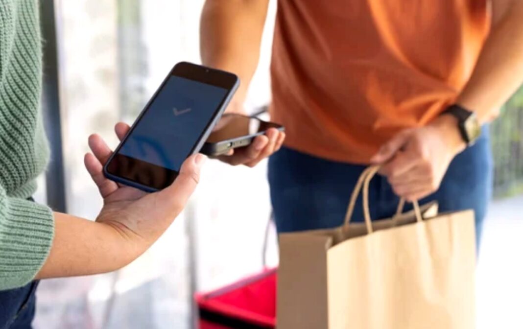 Mobile payment transaction illustrates African directory solutions enabling digital commerce Two people complete a mobile payment transaction outdoors, one holding a smartphone and the other with shopping bags, demonstrating payment-enabled directory solutions for African businesses.