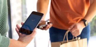 How to plan ahead for money sent to family abroad Two people complete a mobile payment transaction outdoors, one holding a smartphone and the other with shopping bags, demonstrating payment-enabled directory solutions for African businesses.