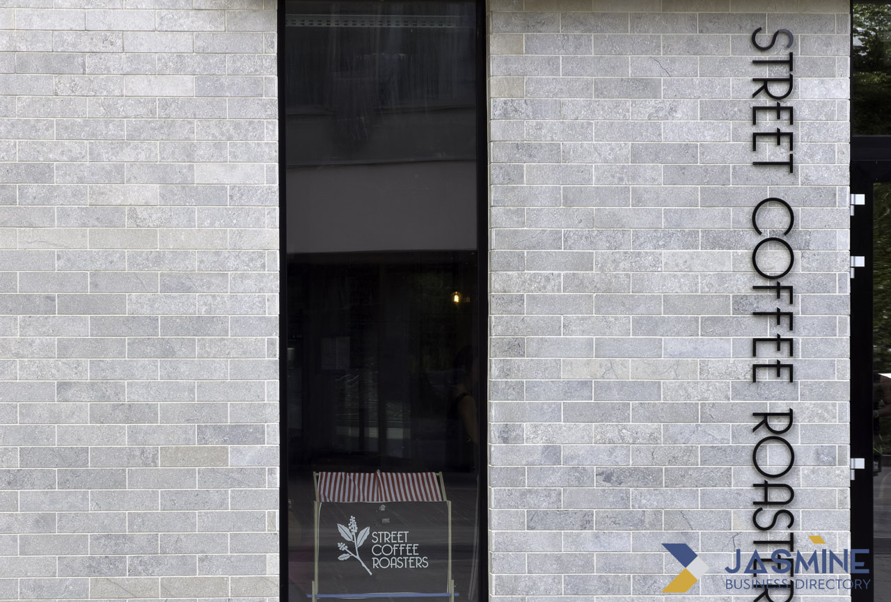 Modern coffee shop storefront with grey brick facade, vertical dimensional signage, and branded packaging at entrance, illustrating cohesive brand identity and visual distinction.