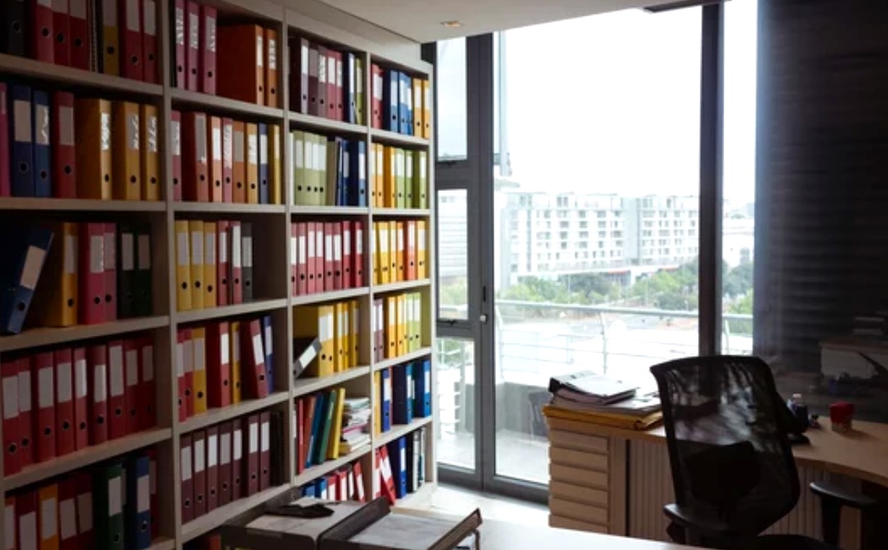 Modern office workspace with floor-to-ceiling shelves of organized multicolored binders and folders, demonstrating the systematic curation approach that marketers apply to business directories.