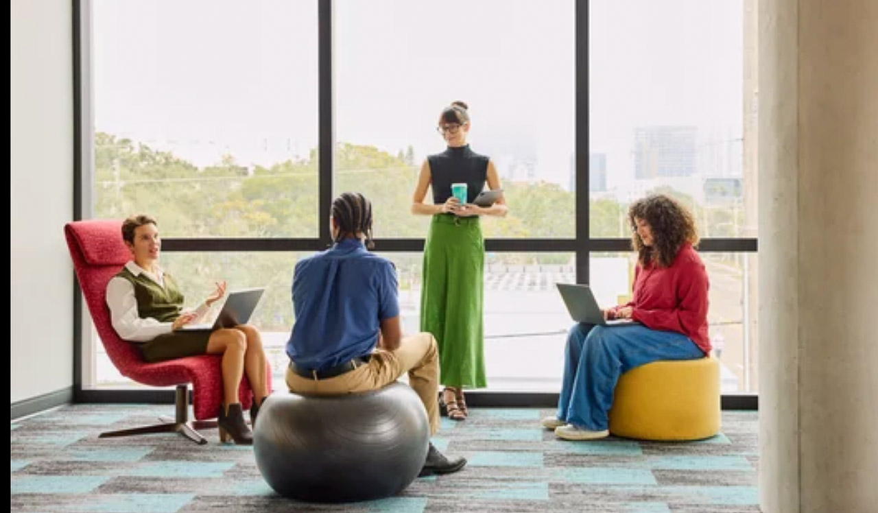 Four professionals collaborate in a modern office with colorful alternative seating and laptops, illustrating the direct team communication approach that parallels email marketing's privacy-focused resurgence.